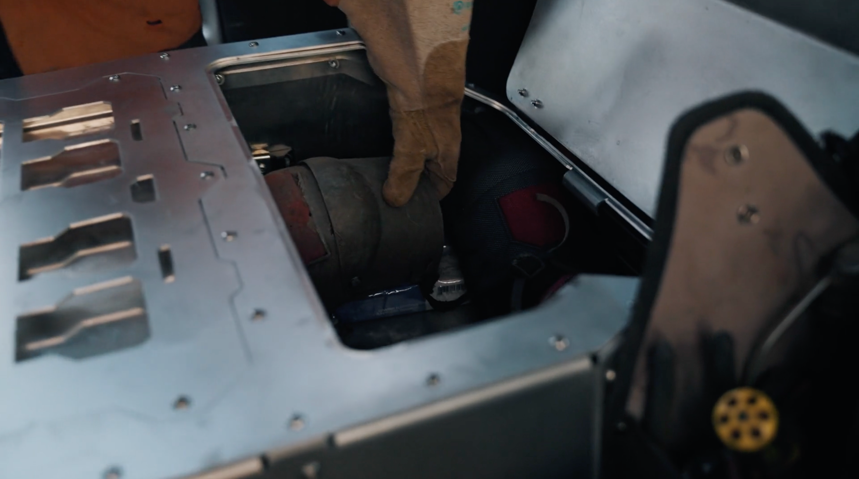 A welder wearing a glove grabbing his welding mask from the storage compartment in his Highway Tight aluminum seat delete system. 