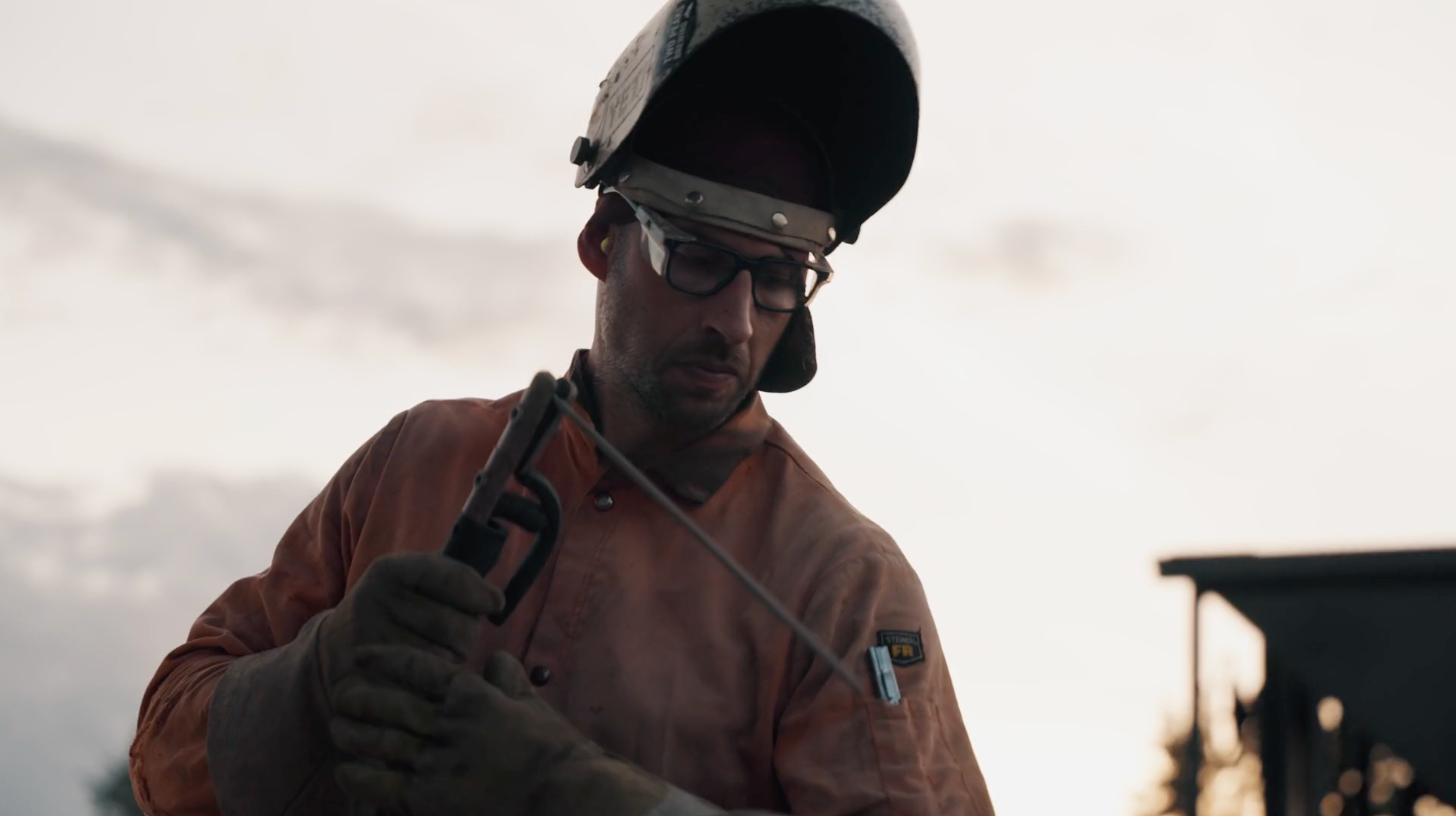 A welder holding a welding tool against a cloudy sky